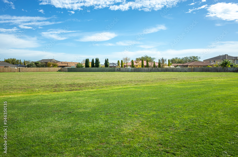 Background texture of a large public local park with green and healthy grass and with some trees and residential houses in the distance. Melbourne, VIC Australia