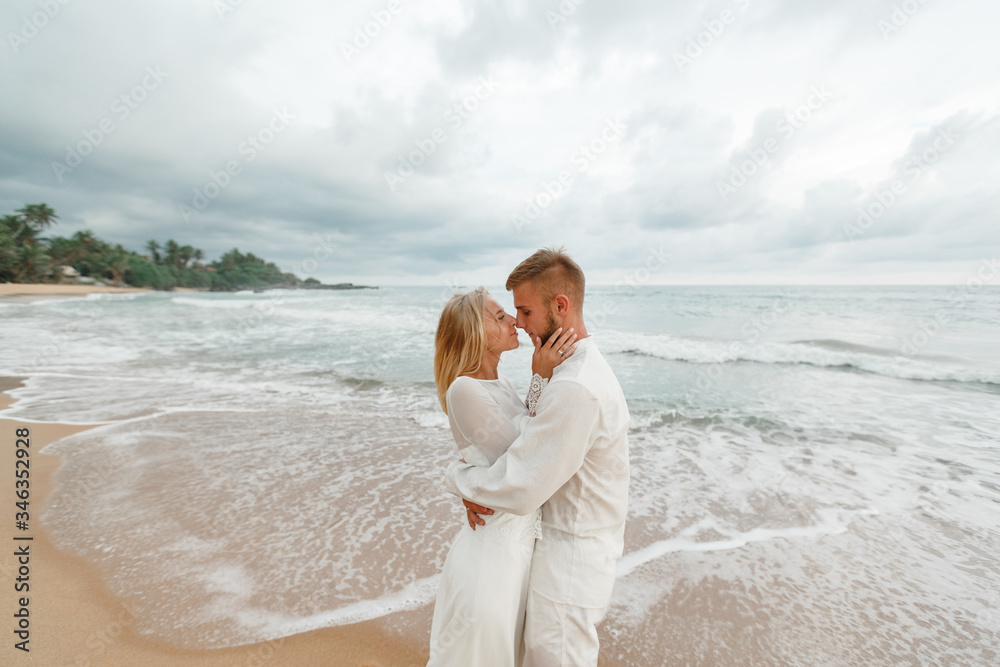 Beautiful wedding couple near the sea. Young couple having tender moments and kissing on the beach at sunset. Man flirting with his woman on romantic holidays in summer time . Love concept