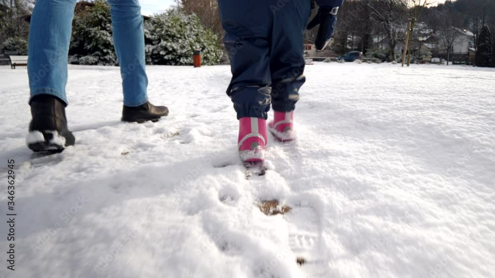 Father and child walking on snow & leaving footprints, close up on legs, tracking shot Father and child walking on snow & leaving footprints, close up on legs, tracking shot