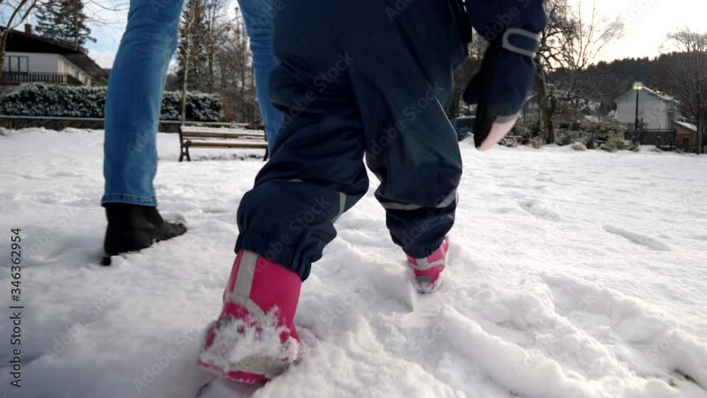 Baby legs following fathers footsteps, walking on snow, wintertime Baby legs following fathers footsteps, walking on snow, wintertime