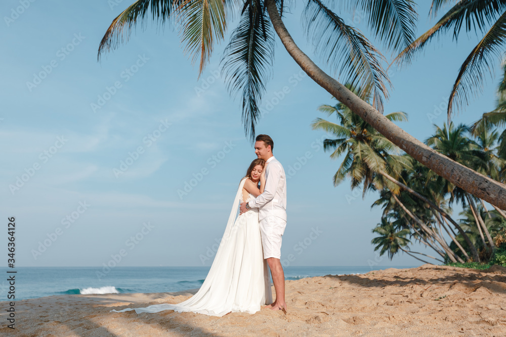 Bride and groom with palm trees on a tropical beach. Wedding by the sea Bride and groom with palm trees on a tropical beach. Wedding by the sea