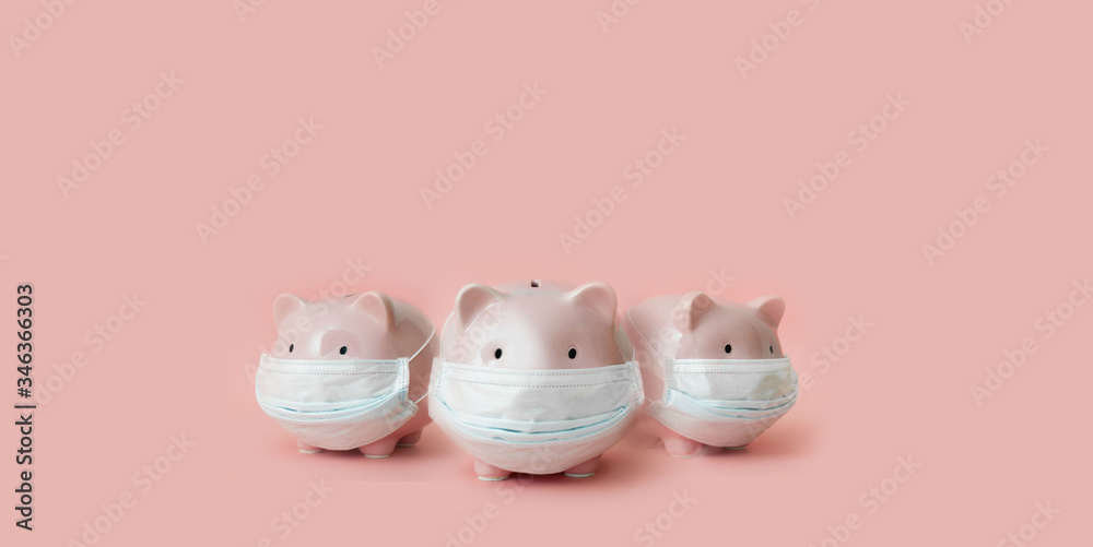 Three piggy banks with medical masks stand on pale pink background Three piggy banks with medical masks stand on pale pink background