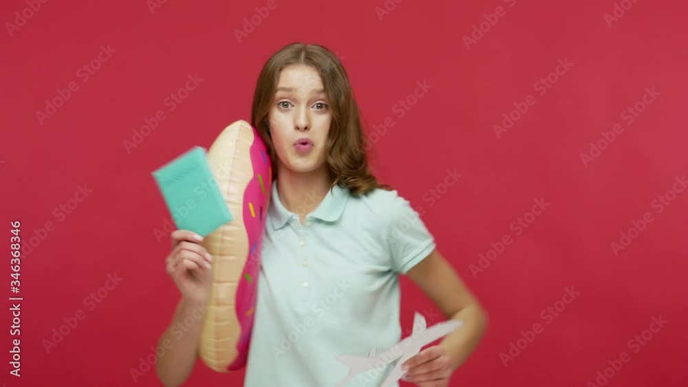 Travel, summer vacation. Happy young woman with rubber ring and passport playing with paper plane, flying and dreaming of trip, visa to foreign countries. indoor studio shot isolated on red background Travel, summer vacation. Happy young woman with rubber ring and passport playing with paper plane, flying and dreaming of trip, visa to foreign countries. indoor studio shot isolated on red background