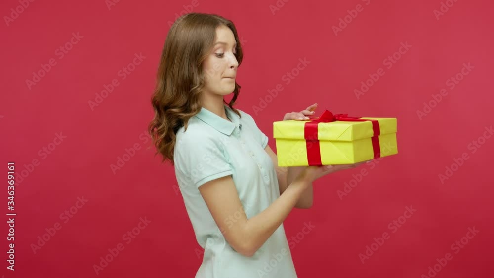 Happy young woman in polo t-shirt carefully unpacking gift, looking inside box with interest and laughing, rejoicing at best present, dream come true. indoor studio shot isolated on red background Happy young woman in polo t-shirt carefully unpacking gift, looking inside box with interest and laughing, rejoicing at best present, dream come true. indoor studio shot isolated on red background