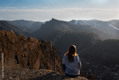A view from the back of a girl sits on a mountain and admires the beautiful view sunset.