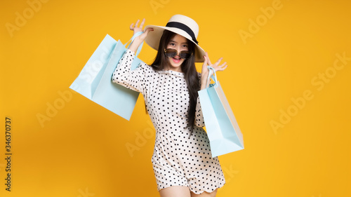 Asian pretty young woman on yellow colour background. She smiling and happy shopping bags. she nice-looking lovely attractive shine .Summer Sale colourful happy time.