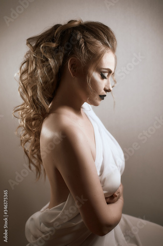 tanned girl with black lips and arrows with light curly hair and professional bright makeup, isolates on white in a silk white dress