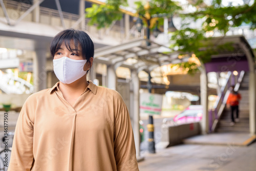 Overweight Asian woman thinking with mask for protection from corona virus outbreak in the city streets outdoors