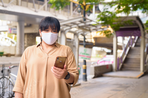 Overweight Asian woman with mask using phone in the city streets outdoors