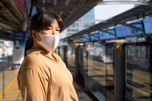 Overweight Asian woman with mask thinking and waiting at the sky train station