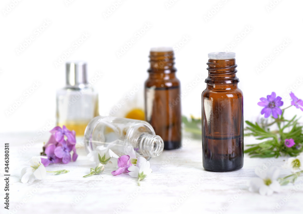 bottles of essential oil and colorful petals of flowers on white table bottles of essential oil and colorful petals of flowers on white table