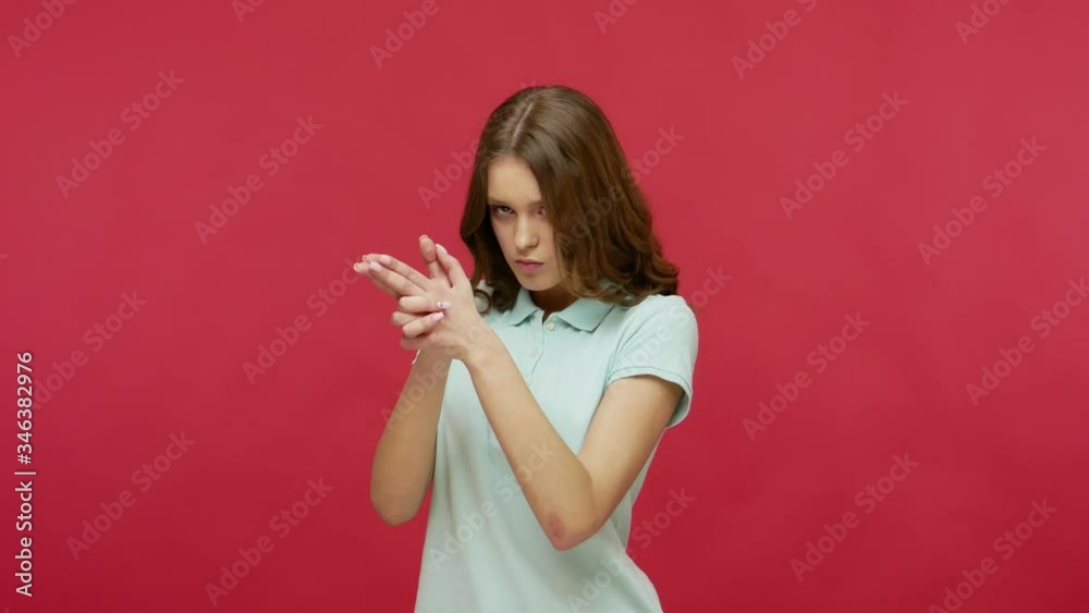 I'll kill you! Dangerous purposeful young woman in polo t-shirt holding gun gesture and searching for target, shooting at camera with finger pistol. indoor studio shot isolated on red background I'll kill you! Dangerous purposeful young woman in polo t-shirt holding gun gesture and searching for target, shooting at camera with finger pistol. indoor studio shot isolated on red background