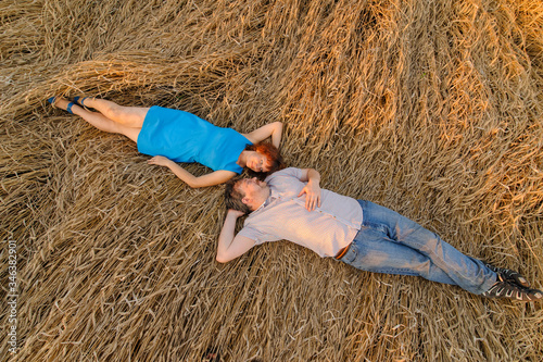 An adult farmer and his wife are lying on rain-covered wheat. A shot taken from the top view.