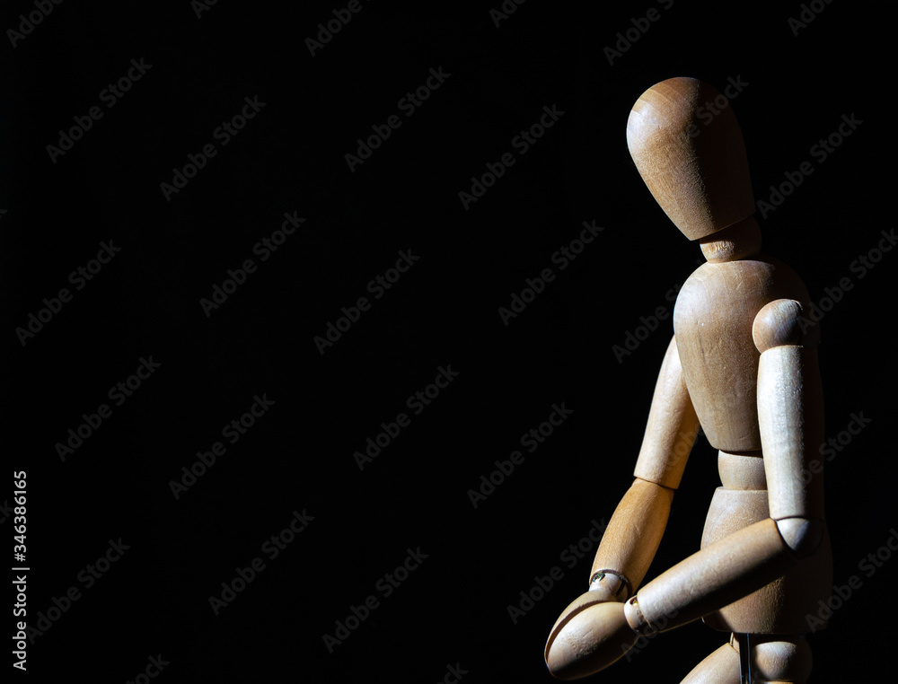 a wooden toy stands with its hands clasped together on a black background a wooden toy stands with its hands clasped together on a black background