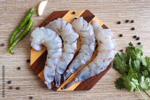 Cleaned, Peeled & Deveined Tiger Prawns or Asian tiger Shrimps. Also known as Kolambi or Bagda chingri. Recipe ingredients like pepper, chilies, garlic, curry leaves at background with copy space.  photo