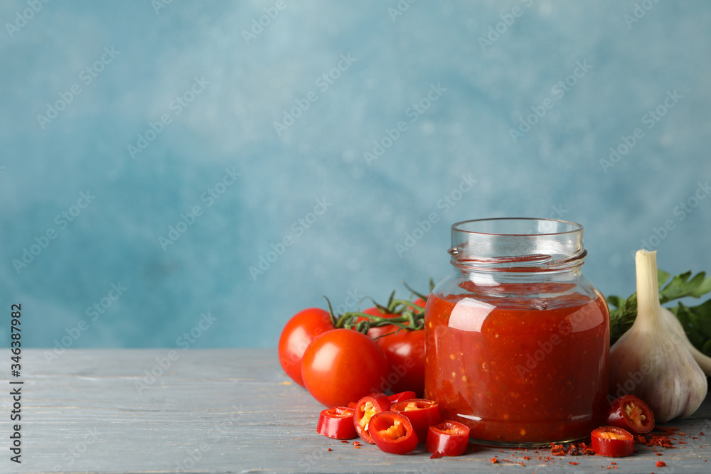 Jar with red chilli and tomato sauce, and spices on wooden table Jar with red chilli and tomato sauce, and spices on wooden table