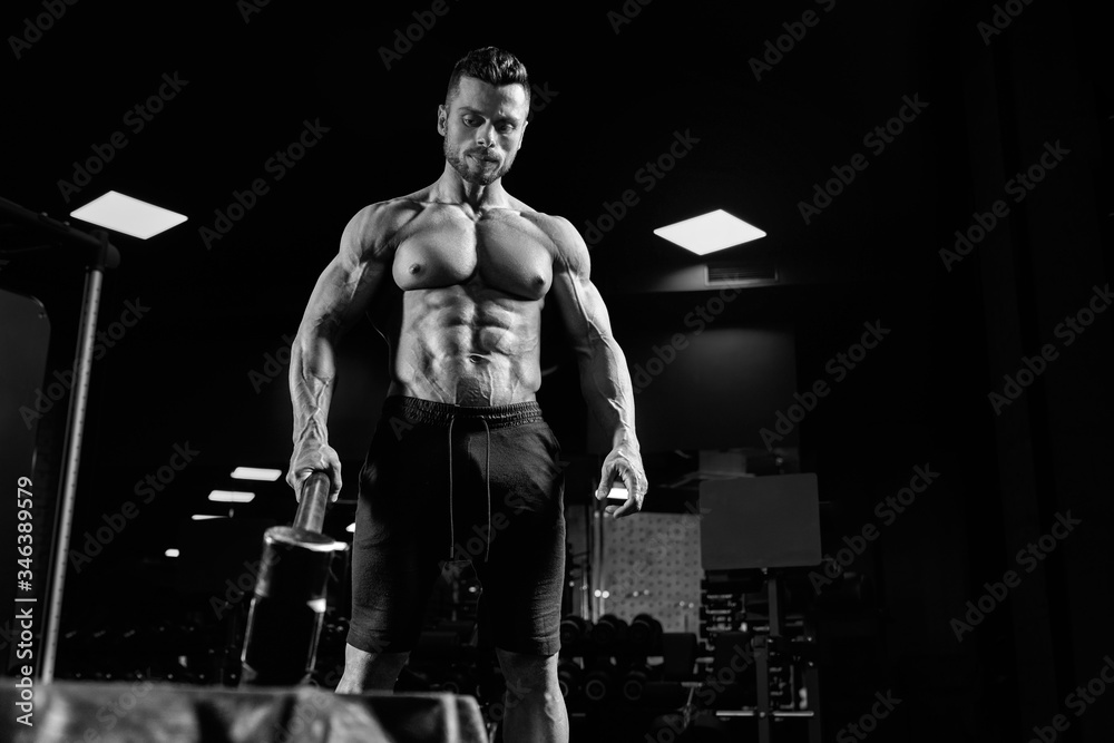 Fototapeta premium Muscular man carrying sledgehammer in gym.