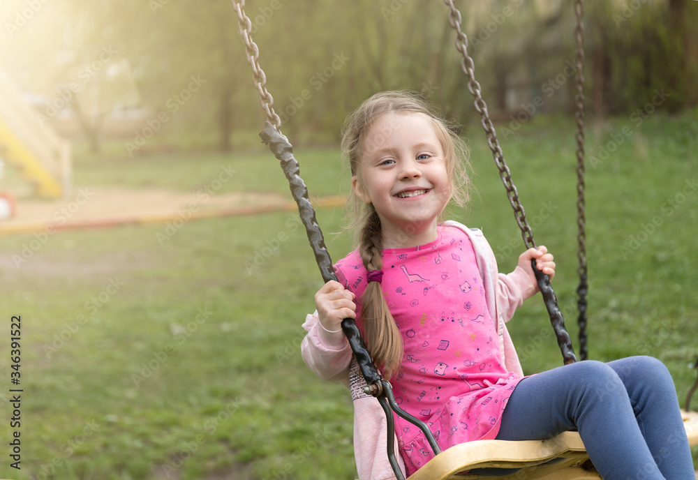 Happy european baby girl laughing and swinging on a swing at a summer playground. Place for text Happy european baby girl laughing and swinging on a swing at a summer playground. Place for text