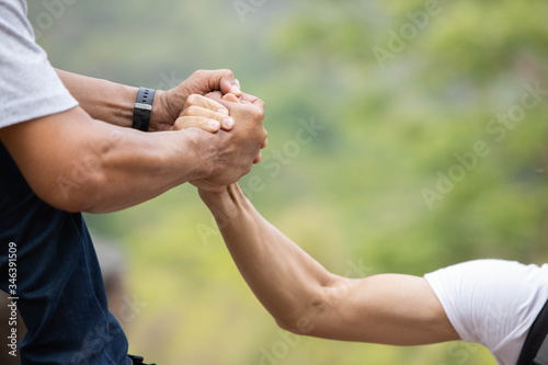 A man helping his friend By pulling hands up on the cliff