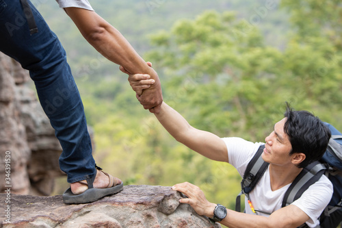 A man helping his friend By pulling hands up on the cliff photo