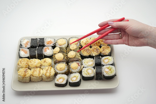 Rectangular plate full of sushi rolls and sticks of red color, on an isolated background, close-up.