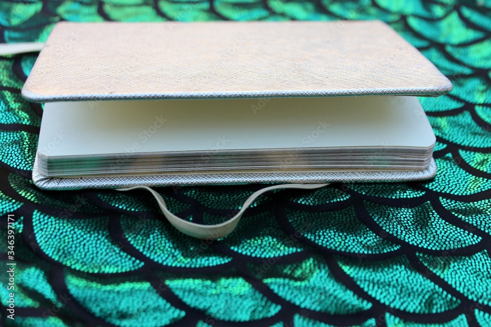 An open notebook on a black-green background imitating scales. Open notebook in a box on a shiny green background with place for text.
