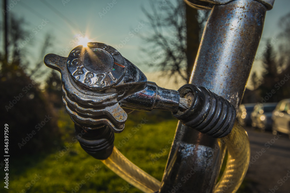 Detail of cheap worn number combination lock on an old bicycle, with sun streak or flare just behind the lock. Park setting or outside in suburb of a city Detail of cheap worn number combination lock on an old bicycle, with sun streak or flare just behind the lock. Park setting or outside in suburb of a city