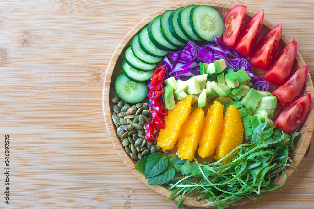 A buddha bowl of fresh summer healthy rainbow salad with cucumbers, tomatoes, arugula, basil, pumpkin seeds, avocado, red cabbage and chilli pepper on a wooden surface A buddha bowl of fresh summer healthy rainbow salad with cucumbers, tomatoes, arugula, basil, pumpkin seeds, avocado, red cabbage and chilli pepper on a wooden surface