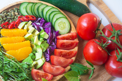 A buddha bowl of fresh summer healthy rainbow salad with cucumbers, tomatoes, arugula, basil, pumpkin seeds, avocado, red cabbage and chilli pepper on a wooden surface