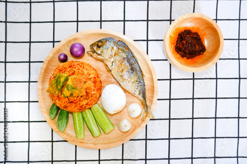 Fried rice with prik pao (Chilli paste with soya bean oil), omelet with cha om, boiled chicken egg, cucumber, eggplant and fried mackerel in wooden plate put on check pixel plaid black and white cloth photo
