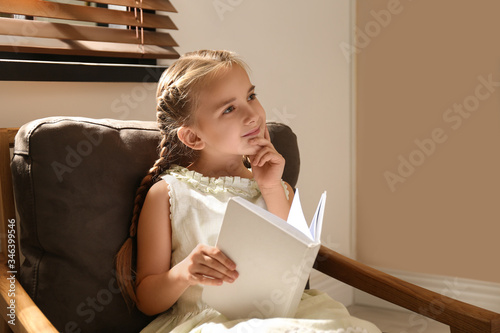Little girl reading book in armchair at home