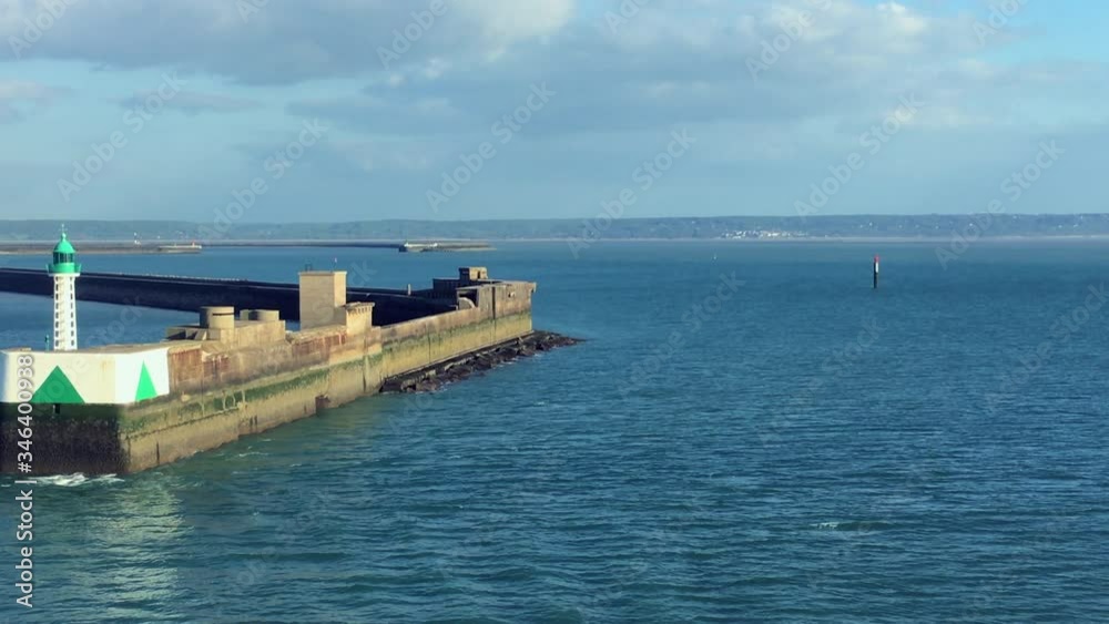 Aerial view passing by historic stone breakwater in French harbor of Le Havre with distinctive lighthouse tower and soaring seagull featuring blue water and coastline in distance. Aerial view passing by historic stone breakwater in French harbor of Le Havre with distinctive lighthouse tower and soaring seagull featuring blue water and coastline in distance.