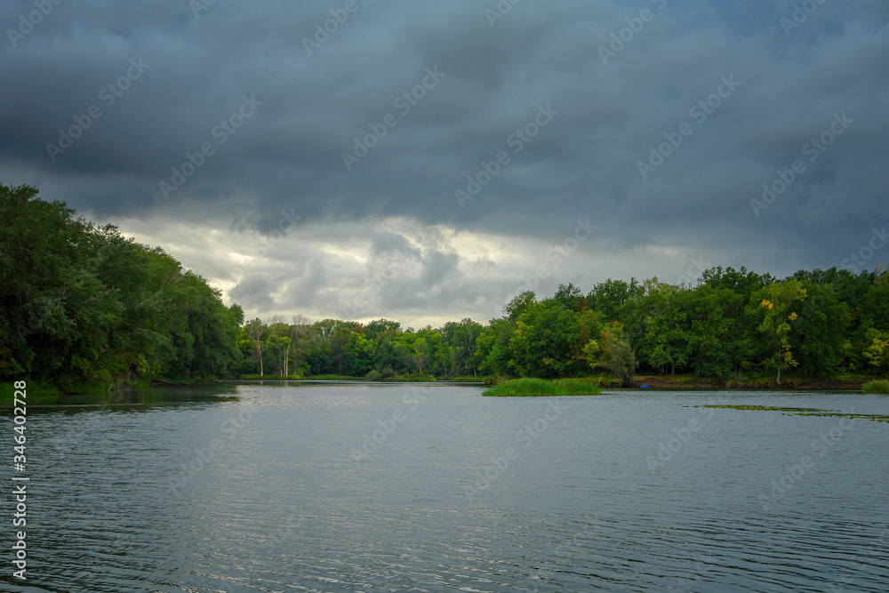 Storm dramatic clouds over a quiet forest lake. Gloomy clouds. Soft focus