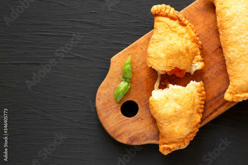 Homemade Deep Fried Italian Panzerotti Calzone with tomato and mozzarella on a rustic wooden board on a black background, top view. Flat lay, overhead, from above. Space for text. photo