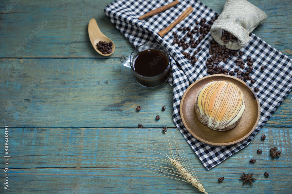 fresh bread put on black scottish pattern fabric with americano in clear cup , sack of roasted coffee beans ,wooden spoon on old wooden table background.Top view with copy space and selective focus. fresh bread put on black scottish pattern fabric with americano in clear cup , sack of roasted coffee beans ,wooden spoon on old wooden table background.Top view with copy space and selective focus.