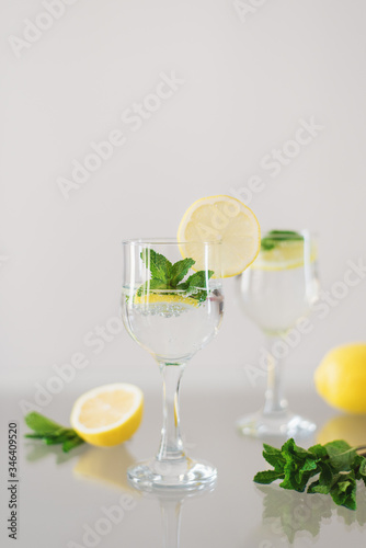 Homemade cocktail with sparkling mineral water, sliced lemon and fresh mint leaves on a glass table. Healthy vitamin drink
