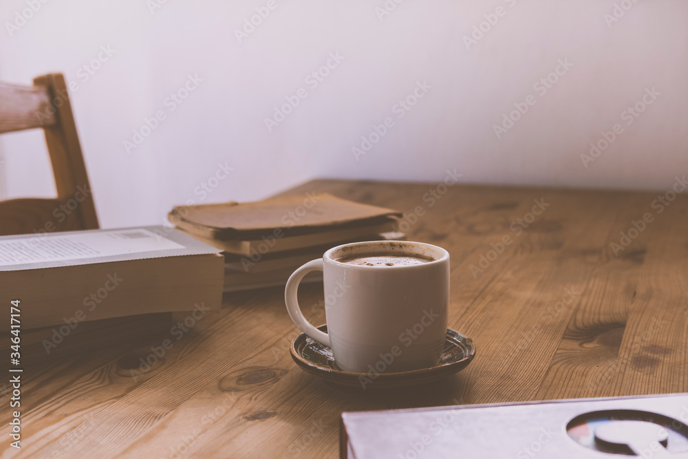 white cup with cappuccino coffee accompanied by a series of books on a rustic wooden table