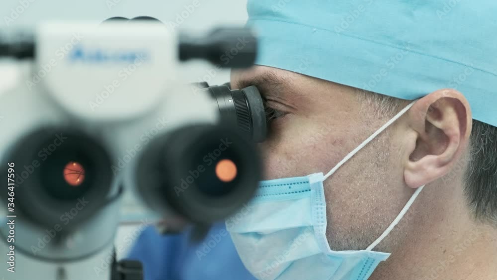 Surgeon looking into the microscope at the eye of female patient at the ...