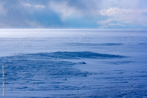 Blizzard on Lake Baikal in winter. Strong wind and a lot of snow. Blue shade of snow. Clouds in the sky. Horizontal.