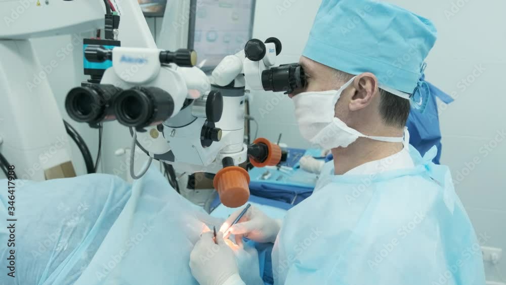 Surgeon looking into the microscope at the eye of female patient at the operating room. Doctor using microscope during eye surgery process, treatment of cataract and diopter correction. 