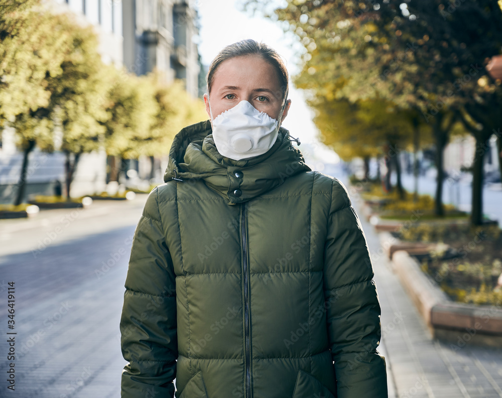 Portrait of a woman in a mask, outside in an empty street, green trees in sunlight on a background. Social distancing during global coronavirus quarantine Portrait of a woman in a mask, outside in an empty street, green trees in sunlight on a background. Social distancing during global coronavirus quarantine