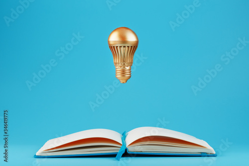 A Golden light bulb in levitation from an open notebook on a blue background. Concept of the idea.