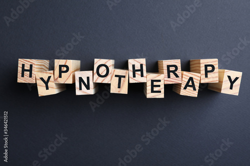 Wooden blocks with word HYPNOTHERAPY on black background, flat lay