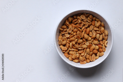 Peanuts in a white bowl on a white background, seen from above, with copy space