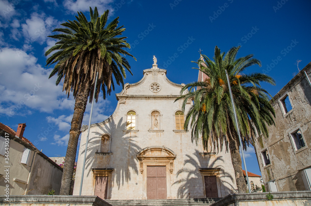 Croatian seaside town, Dalmatia, medieval Roman Catholic church with palm trees with blue sky in summer sunshine.