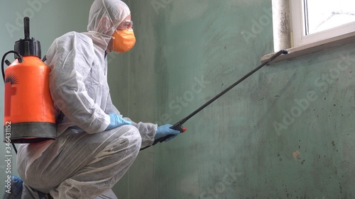 A man in a protective suit, glasses and a respirator sprays a disinfectant. Spraying disinfectants in public spaces against Coronavirus. Cleaning, Sanitising and Disinfecting photo