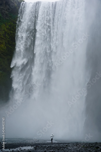 Person is walking under the water and mist of Seljalandsfoss waterfall in Iceland 