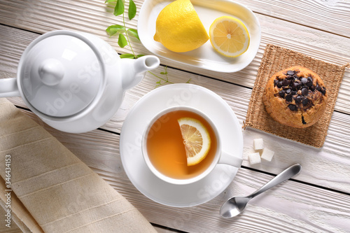 Top view of a cup of tea with lemon and cupcake on white table