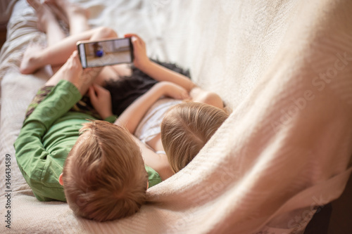 kids play telephen, watch videos on gadgets lying on the couch