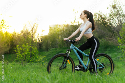 Young nice woman has a bike ride in a park on sunset. copy space